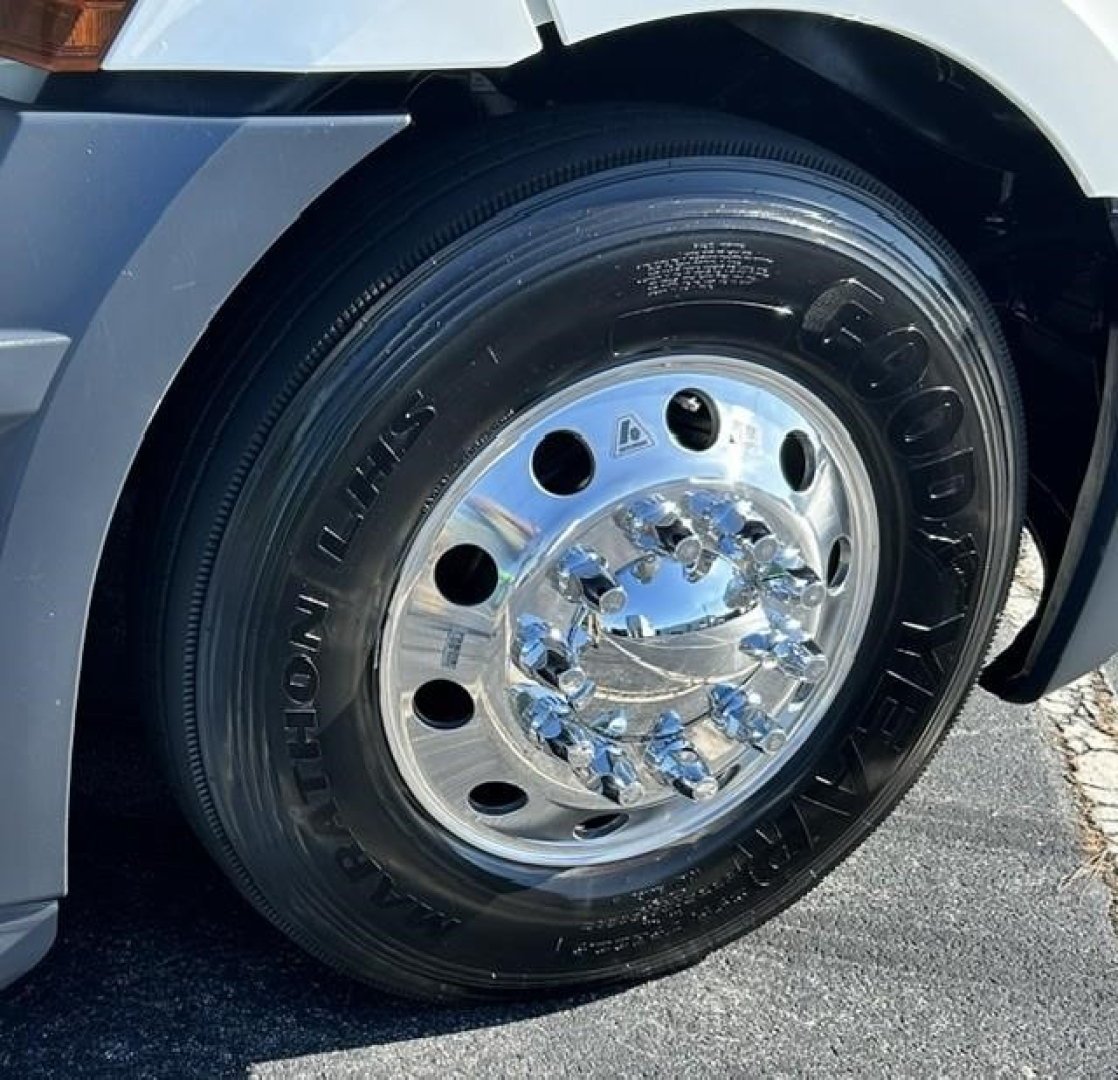 Wheel close-up on a Freightliner Cascadia showing a polished chrome rim and Goodyear tire; visible text on tire reads 'Goodyear' and other tire markings.
