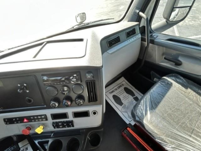 Cab interior of a Freightliner Cascadia 126 day cab showing dashboard controls, steering column, and passenger seat with plastic cover.