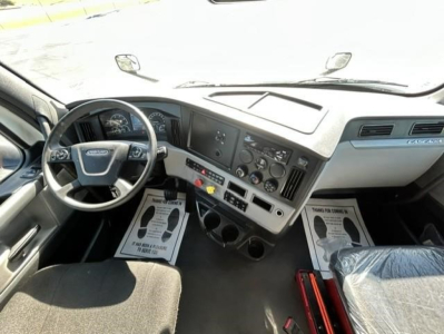 Cab interior of Freightliner Cascadia 126 day cab showing steering wheel, dashboard with gauges, center console, and front passenger seat.