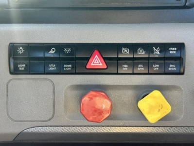 Dashboard switches and controls on Freightliner Cascadia dash showing light test, utility light, dome light, hazard button, HSA OFF, ATC SPIN, LDW OFF, ENG SHDN, and large red and yellow knobs.