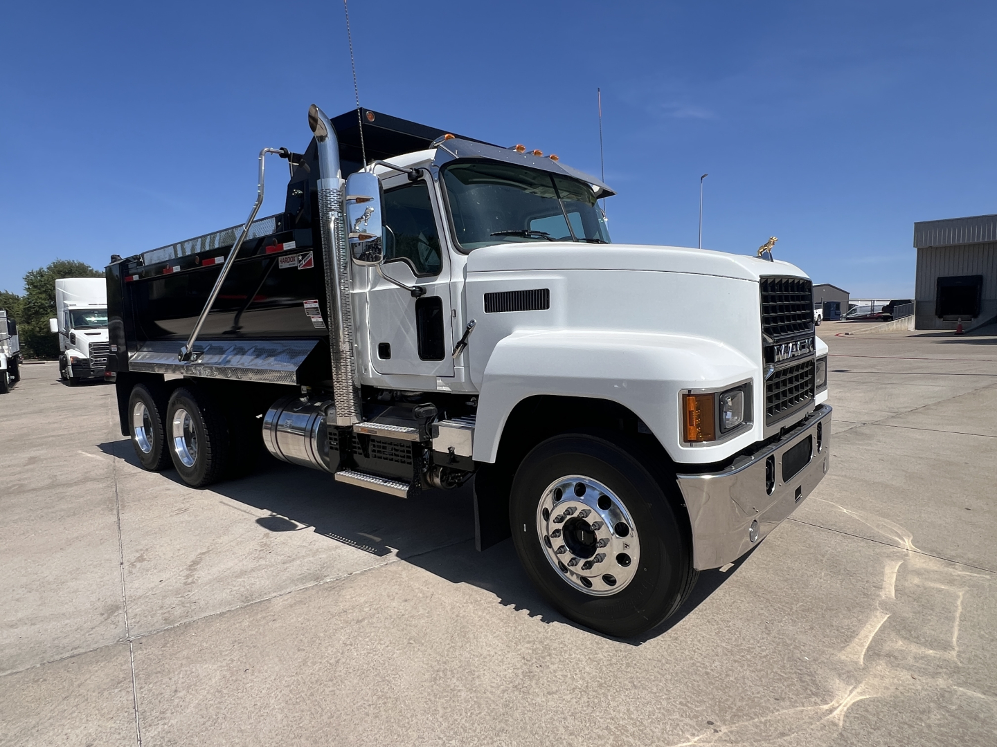 New 2027 Mack PI64 dump truck side view showing front grille, cab, wheels, and dump bed with chrome steps.
