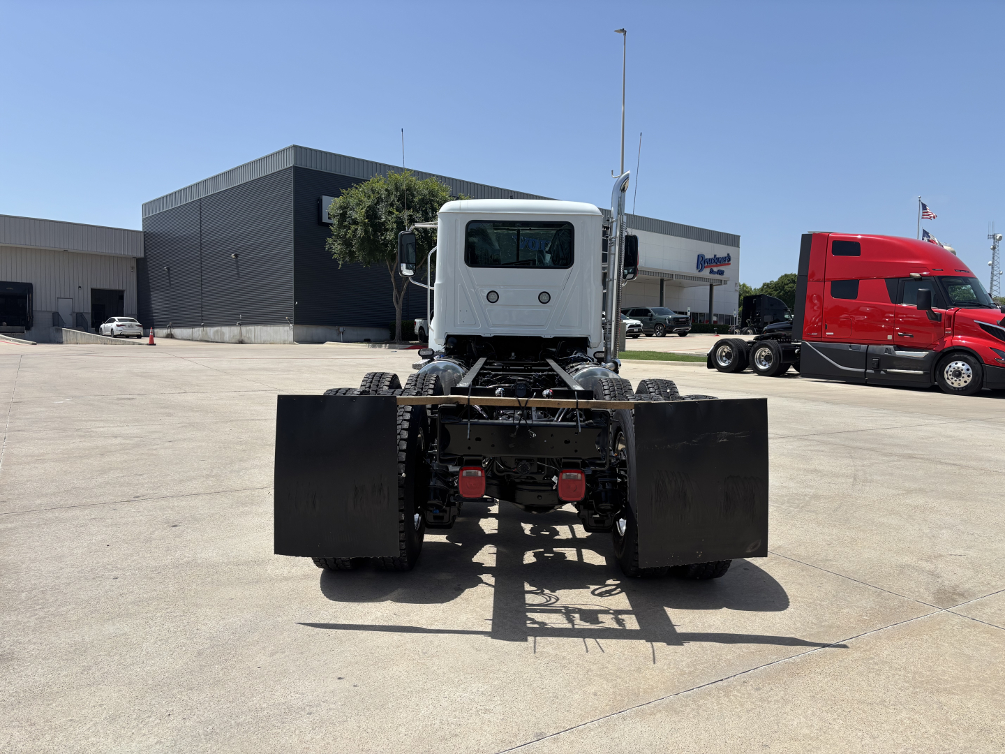 Dump truck chassis rear view showing dual rear axles and black blade-style components with white cab, Mack PI64 model.