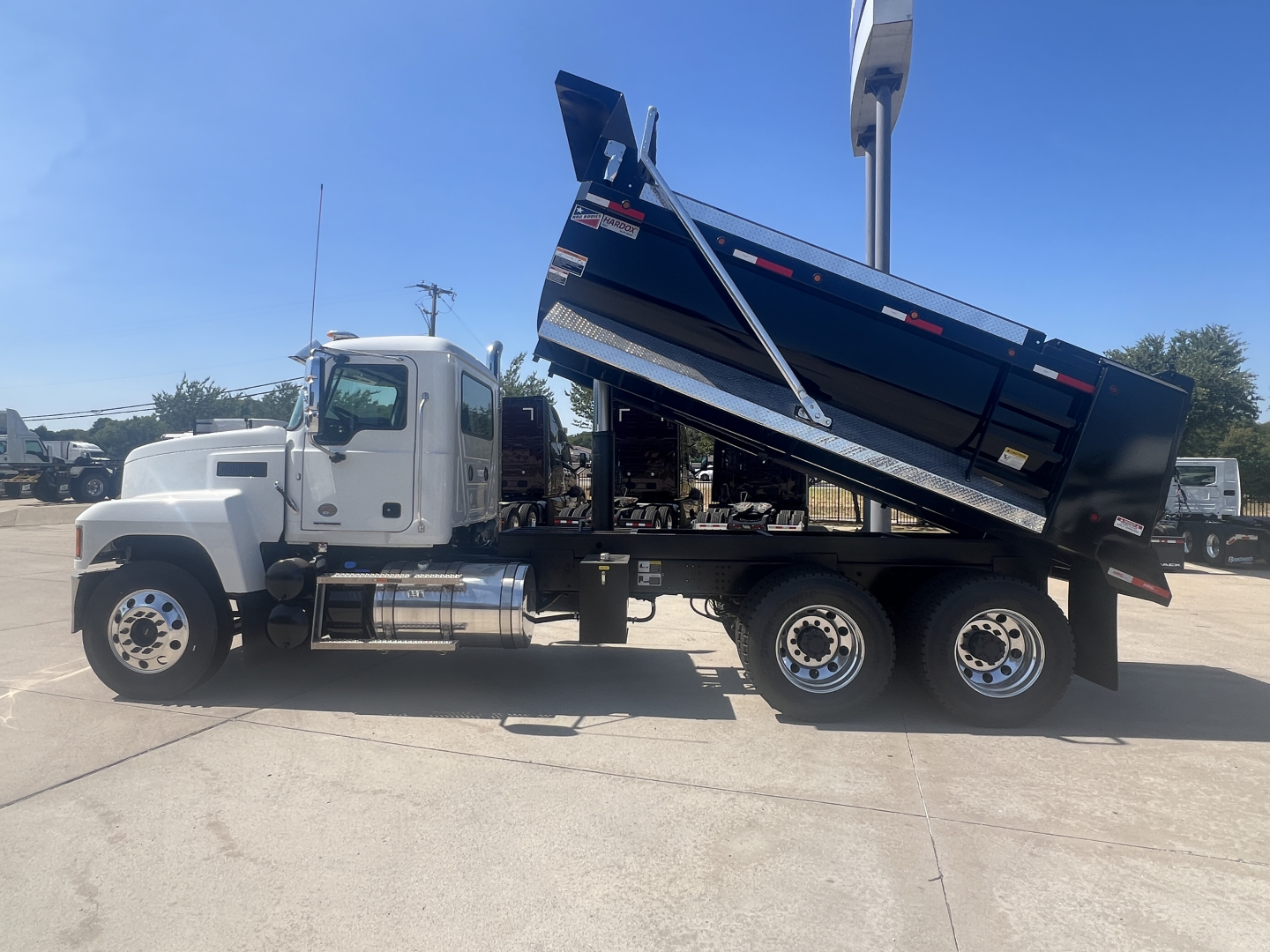 Dump truck with a raised blue bed and white cab, all-wheel drive, images shows side profile of Mack PI64 ready for service.