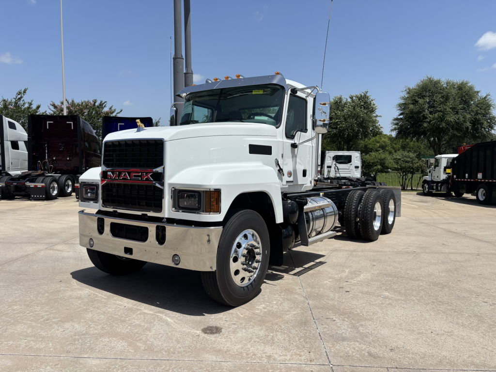 Mack PI64 dump truck front-right view showing white cab, chrome bumper, dual rear wheels, fuel tanks, and Mack grille.