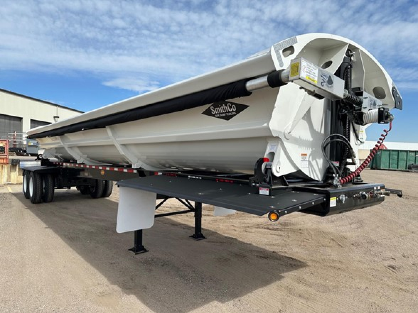 Smithco air ride side dump trailer in view showing hydraulic ram and white hopper with SmithCo logo.
