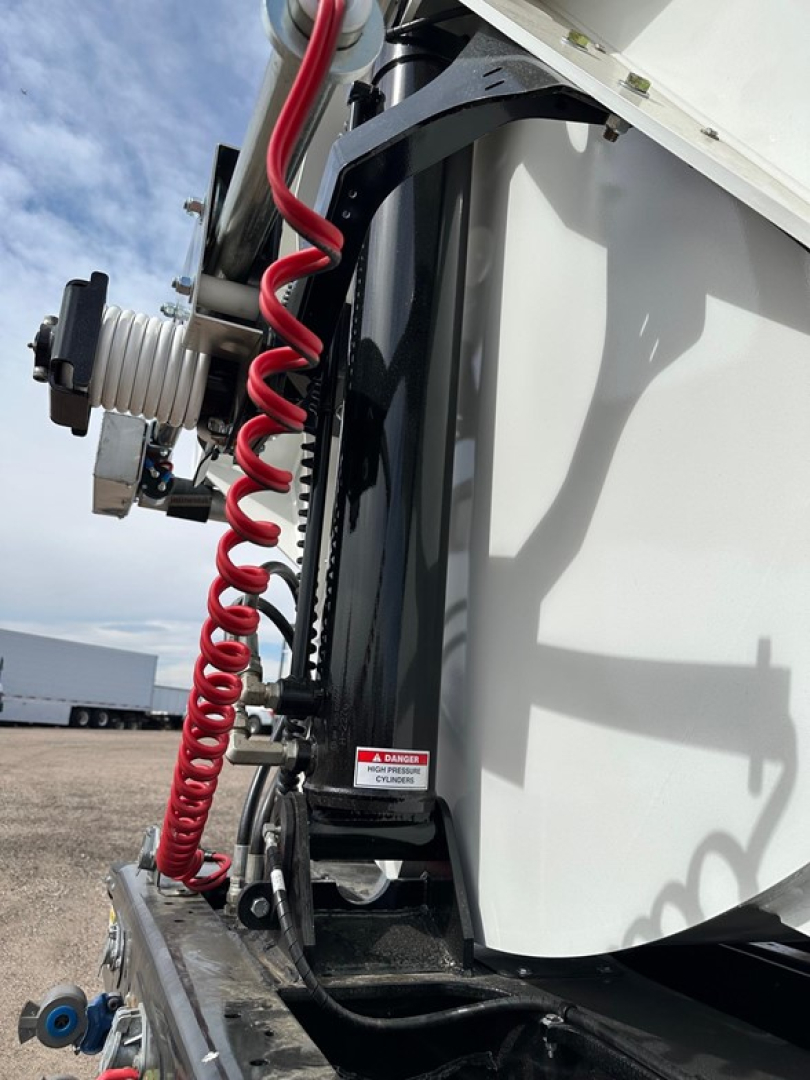 Air ride side dump trailer showing coiled air hose and hydraulic components with control valve and warning label.