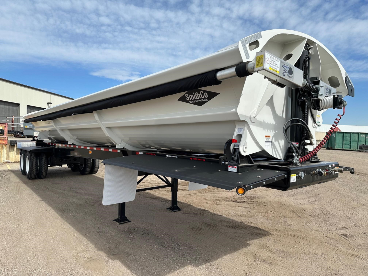 SmithCo air ride side dump trailer showing hydraulic system and white dump body with SmithCo logo, silver hitch, and dual-axle configuration.