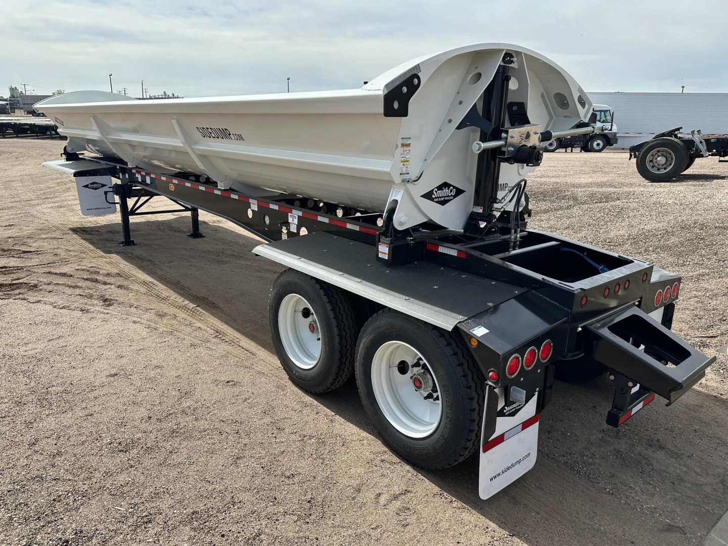 Smithco air ride side dump trailer on a dual-axle trailer chassis showing hydraulic cylinder and tailgate area with reflective tape.