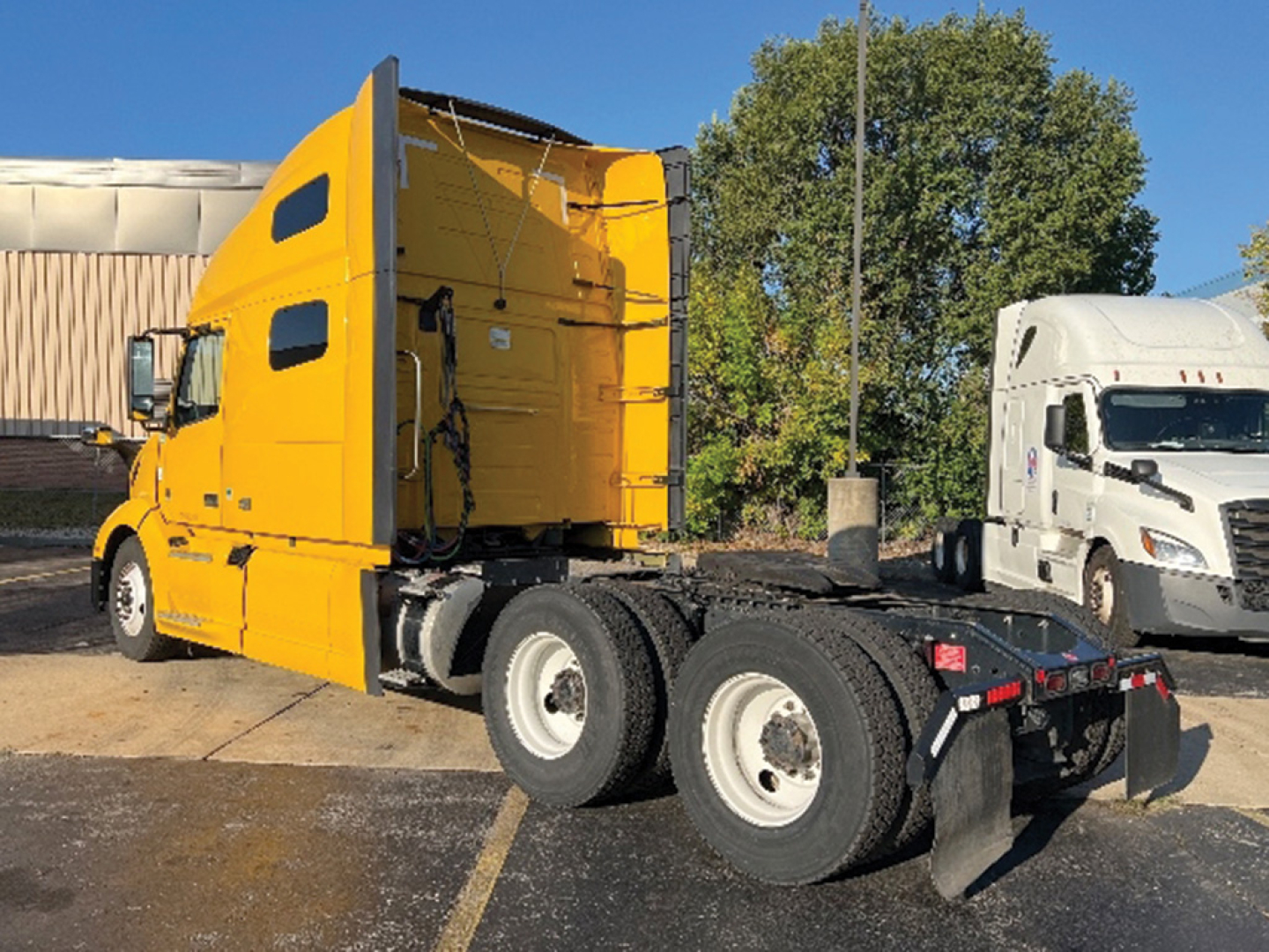 Truck side view showing a bright yellow Volvo VNL 760 sleeper tractor with a 6x4 rear axle configuration, empty trailer connection area, and black fenders.