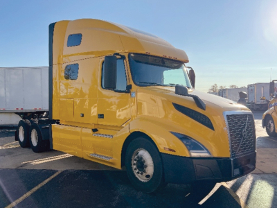 Volvo VNL 760 sleeper cab tractor in yellow with black grille, side mirrors, and window; shows front and passenger side; no visible text on the truck itself.