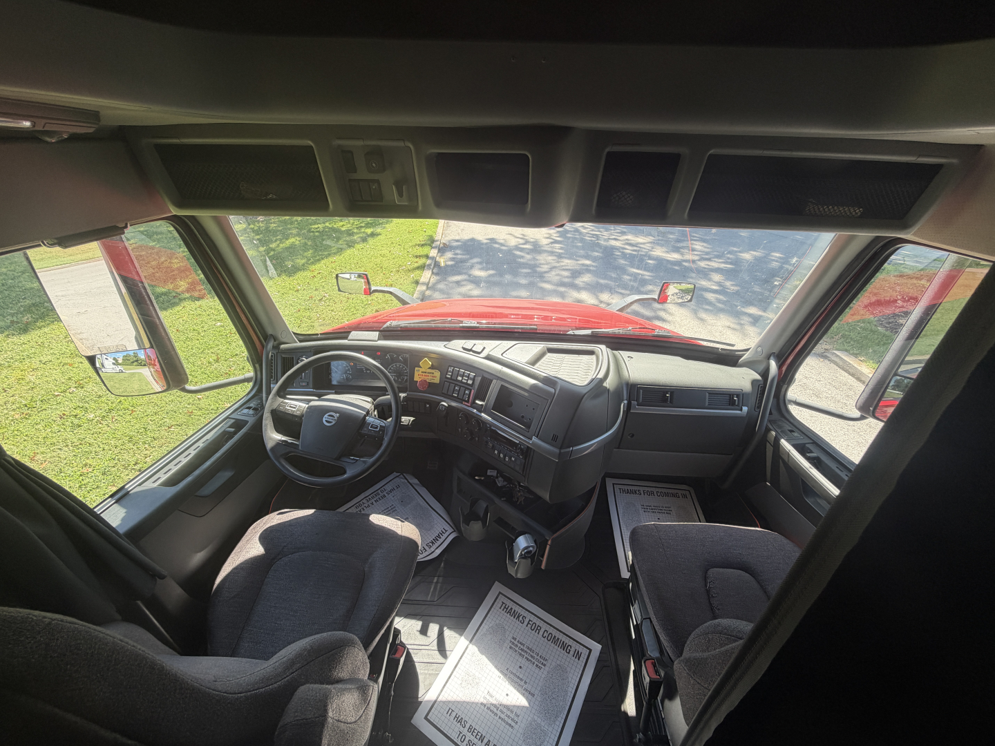 Truck cab interior showing steering wheel, dashboard, and front seats of a 2022 Volvo VNL64T760 sleeper, with driver’s seat on left and passenger bench.