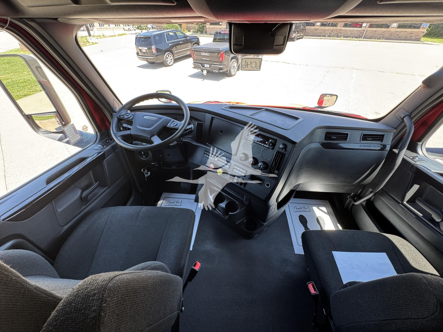 Truck cab interior of a Freightliner Cascadia 126 showing the dash, steering wheel, and front seats with a center console and paperwork on the passenger floor.