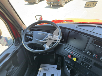 Cab interior of a Freightliner Cascadia truck with steering wheel, dashboard, and center console; visible text includes none clearly legible on the dashboard.