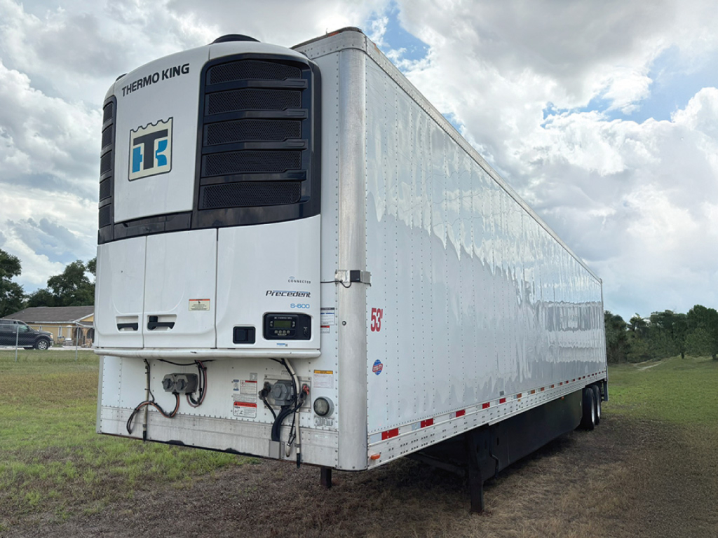 Utility aluminum reefer trailer with Thermo King unit on front, white with branding, side racks, and red reflective tape along lower edge.