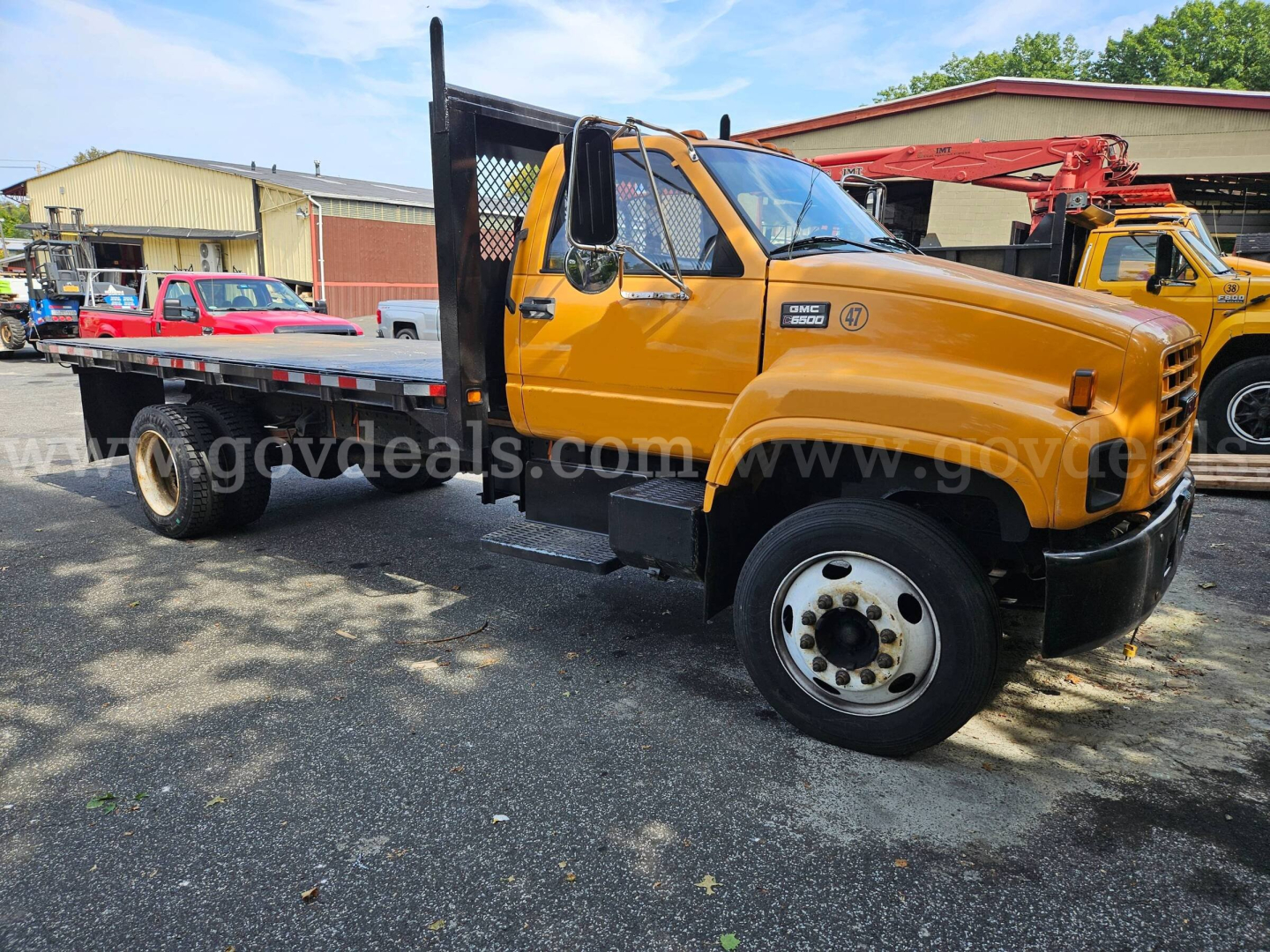 1998 GMC C6500 flatbed dump truck side view showing yellow cab and black flatbed with metal diamond plate. VIN tag not visible, stock number 32136-35 in lot.