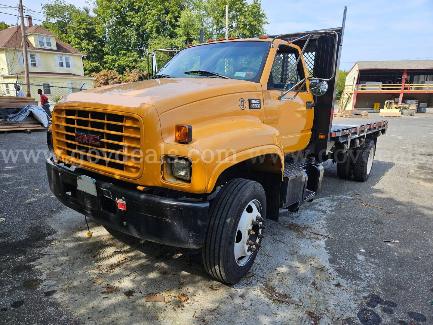 GMC C6500 flatbed dump truck in orange showing front grille and dual rear axles with cab doors open