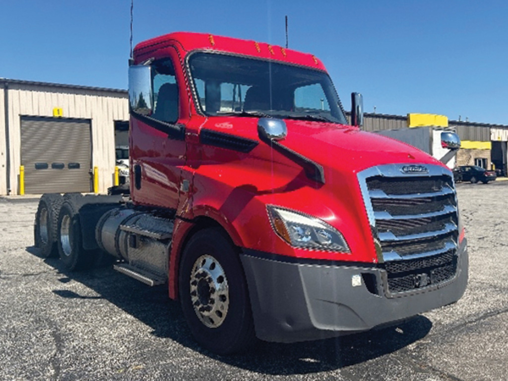 Red Freightliner Cascadia 126 daytime cab truck in a lot, front three-quarter view, with chrome grille and large bumper.