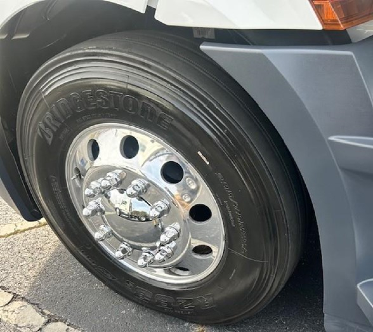 Bridgestone heavy truck front wheel and tire showing chrome hub with lug nuts and fender.
