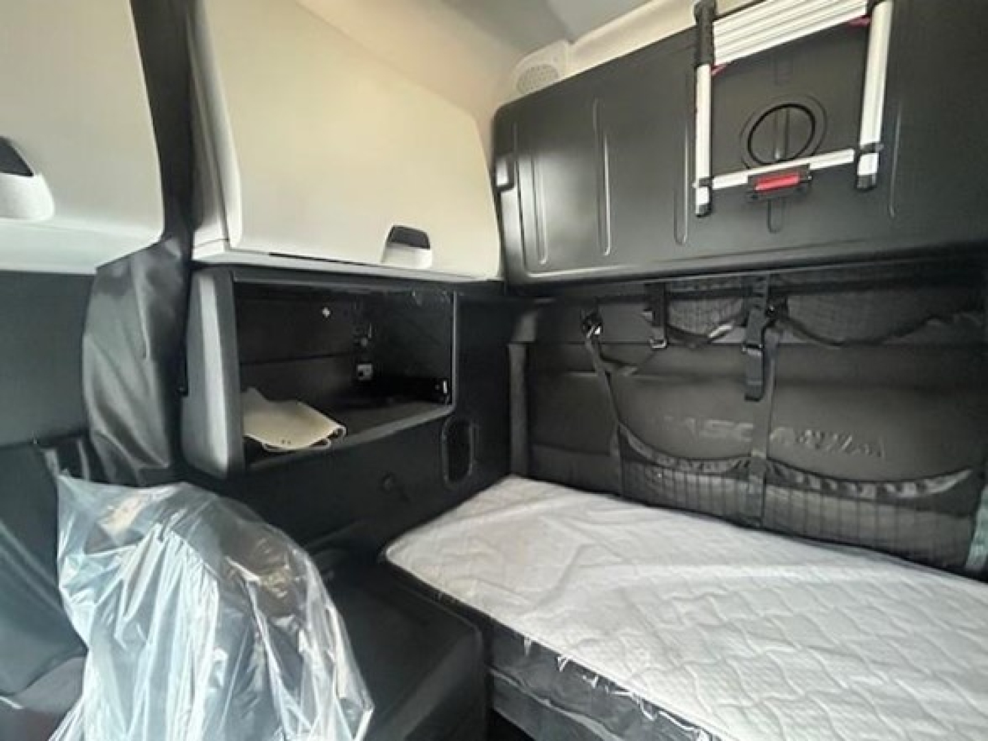 Truck sleeper cabin interior of a 2023 Freightliner Cascadia 126 showing storage compartments, bunk bed with quilted mattress, and overhead cabinet.