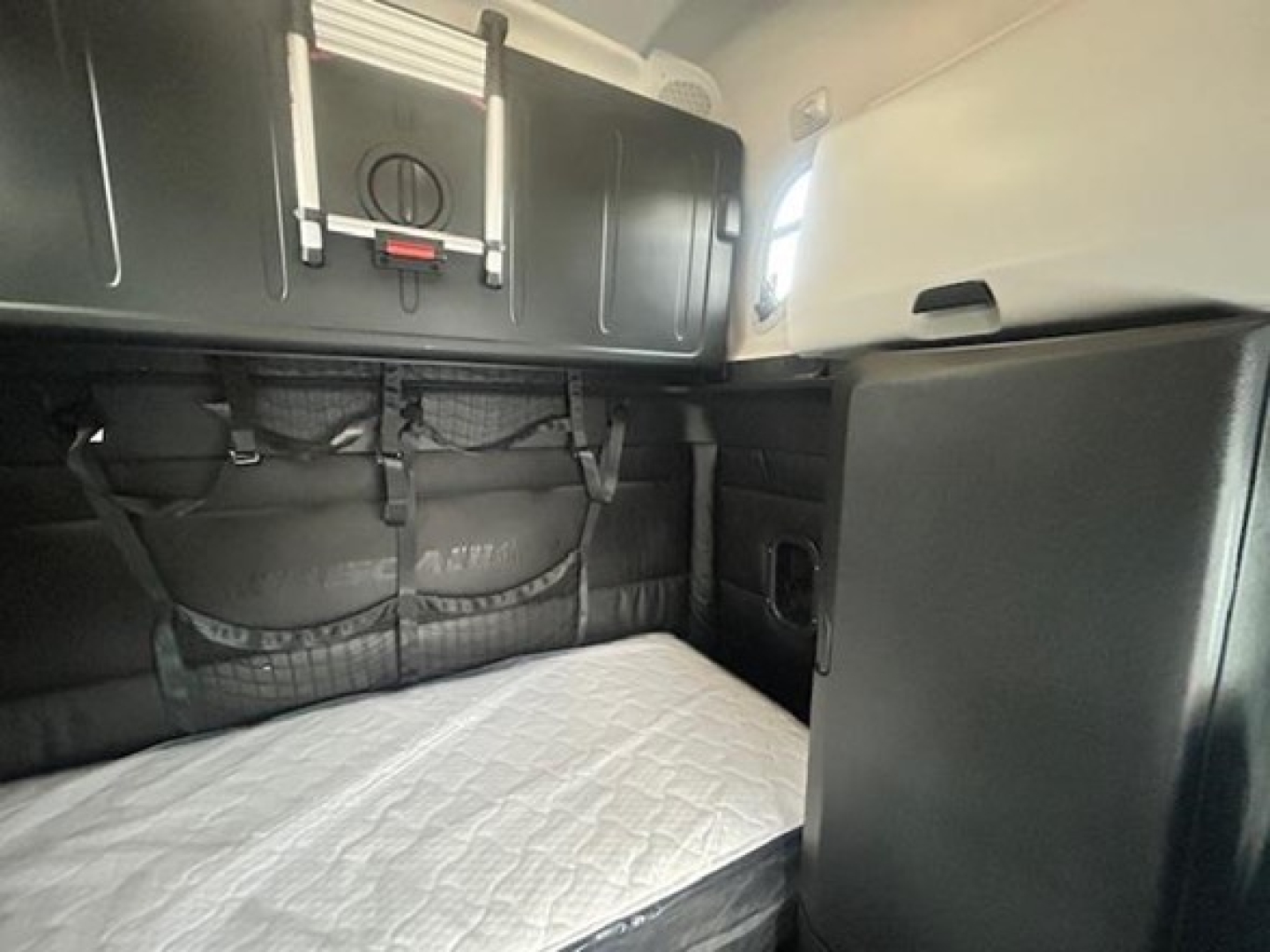 Freightliner Cascadia 126 sleeper cab interior showing bunk area with storage nets and overhead cabinets.