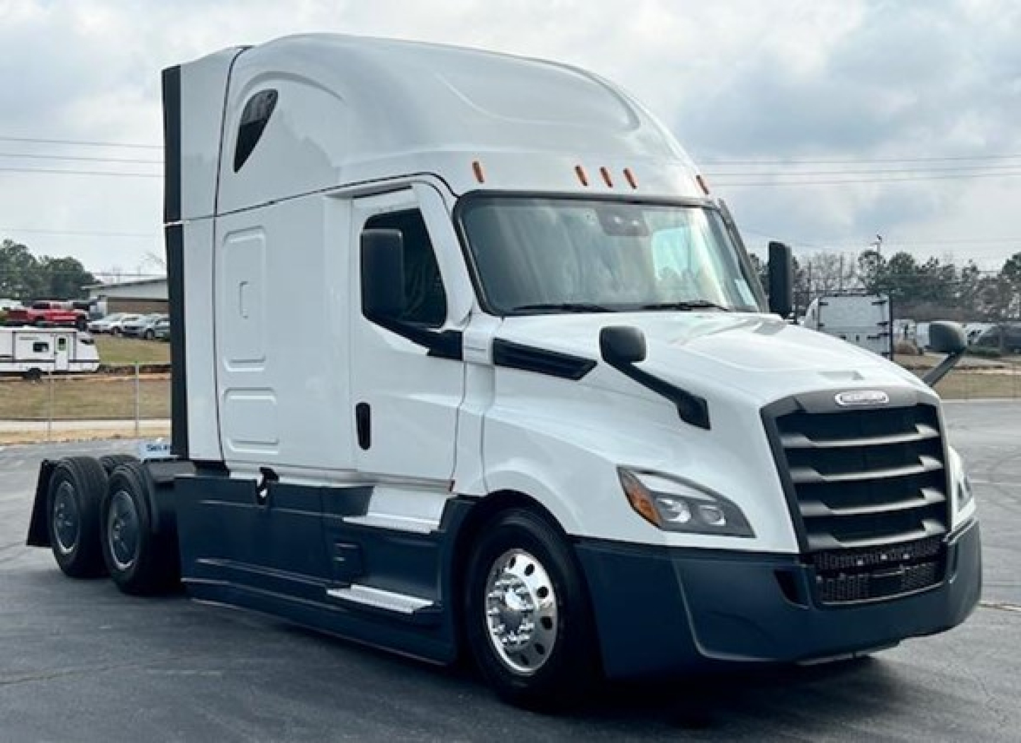 Conventional sleeper Freightliner Cascadia 126 truck in white and dark blue, side view showing sleeper cab, dual rear axles, and chrome wheels.