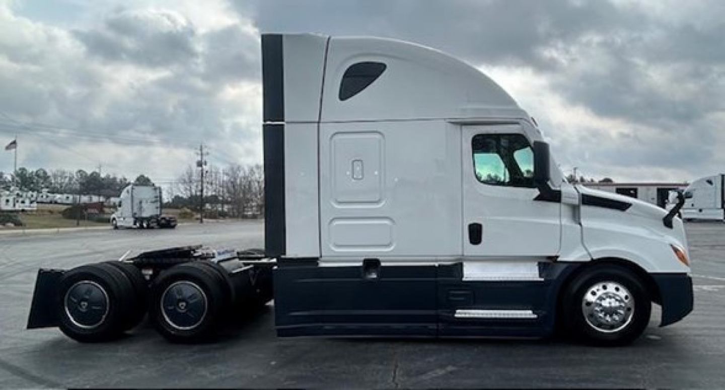 Truck side view showing a white Freightliner Cascadia 126 sleeper with black lower cab panels and dual rear axles.