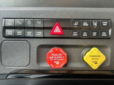 Truck dash panel with multiple control buttons, red hazard triangle button, red trailer air supply knob, and yellow parking brake knob.