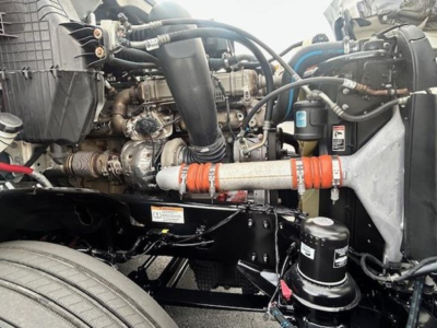 Diesel engine bay of a Freightliner Cascadia 126 showing engine components, hoses, and a cylindrical canister; visible labels and wiring.