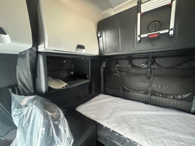 Truck sleeper cabin interior of a 2023 Freightliner Cascadia 126 showing storage compartments, bunk bed with quilted mattress, and overhead cabinet.