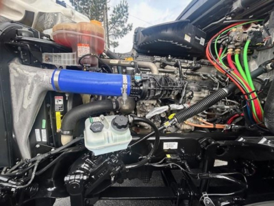 Freightliner Cascadia engine bay showing coolant reservoir, blue silicone intercooler hose, and multiple colored wires in engine compartment.