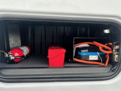 Trunk of a Freightliner Cascadia with a red emergency fire extinguisher, red storage box, and orange portable power pack in the front storage compartment.
