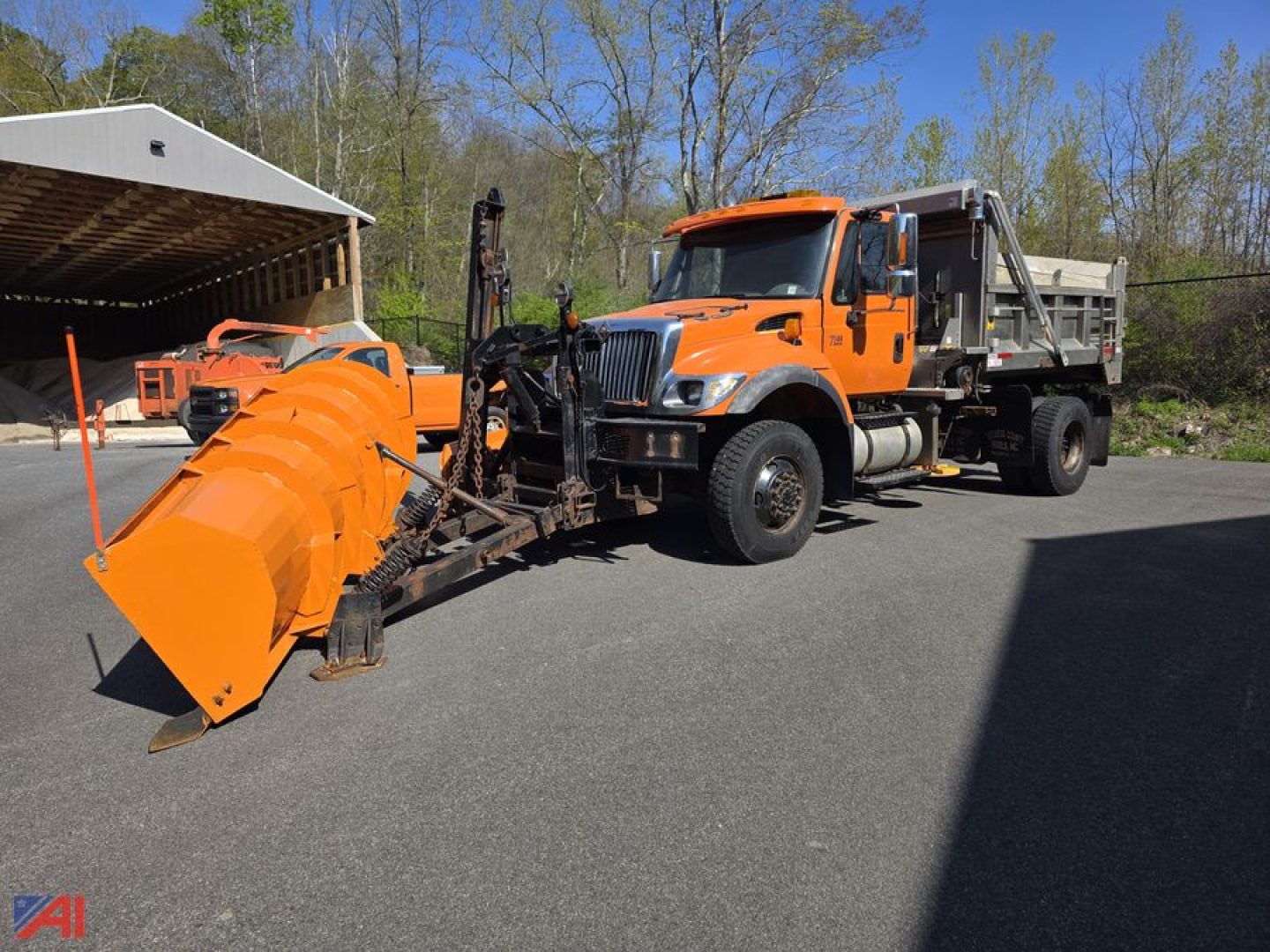 Orange 2006 International WorkStar 7500 dump truck with a plow and wing attachment parked on asphalt; aluminum snow plow and sander equipment connected to front; orange cab and dump bed visible.