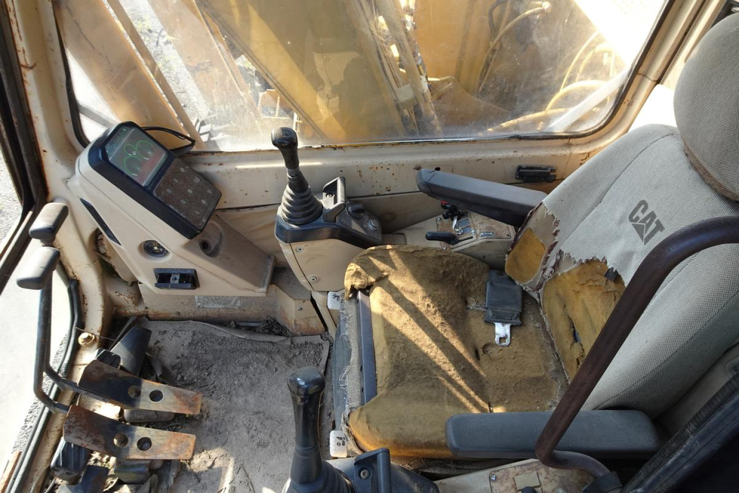 Caterpillar 312 excavator cabin interior showing control joystick, monitor, and worn seat with yellow fabric and Cat branding.