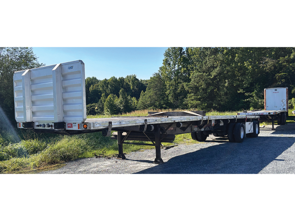 Flatbed trailer with aluminum and steel composite deck showing storage box and rear wheels.