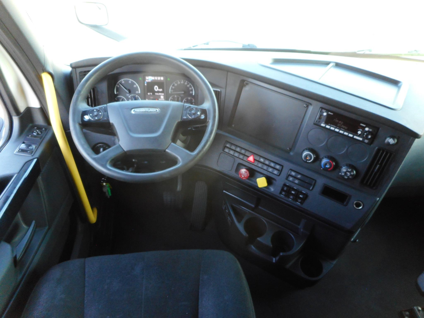 Freightliner Cascadia 126 truck cabin interior showing steering wheel, dashboard with gauges, infotainment screen, and control buttons from the driver’s seat perspective.