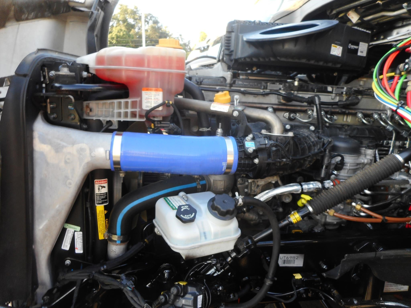 Freightliner Cascadia 126 engine bay showing coolant reservoir, blue hose, windshield washer style reservoir, and various cables.