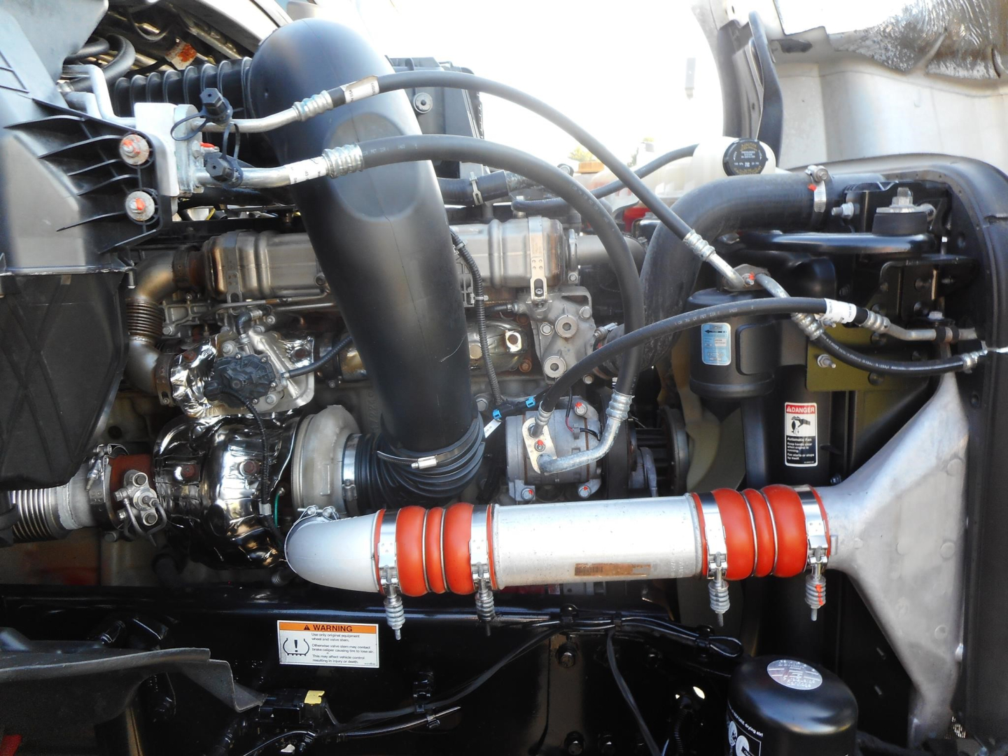 Freightliner Cascadia engine bay showing turbo hoses, intercooler piping, coolant reservoir, and brass-colored engine components.