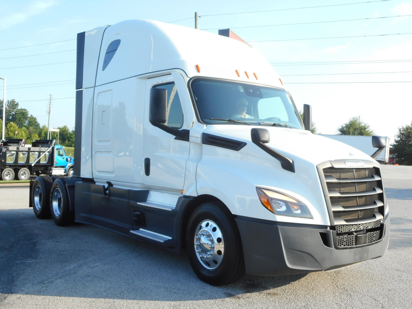 Truck cab showing 2024 Freightliner Cascadia 126 sleeper with white paint, black grille, and side mirrors; front right view.