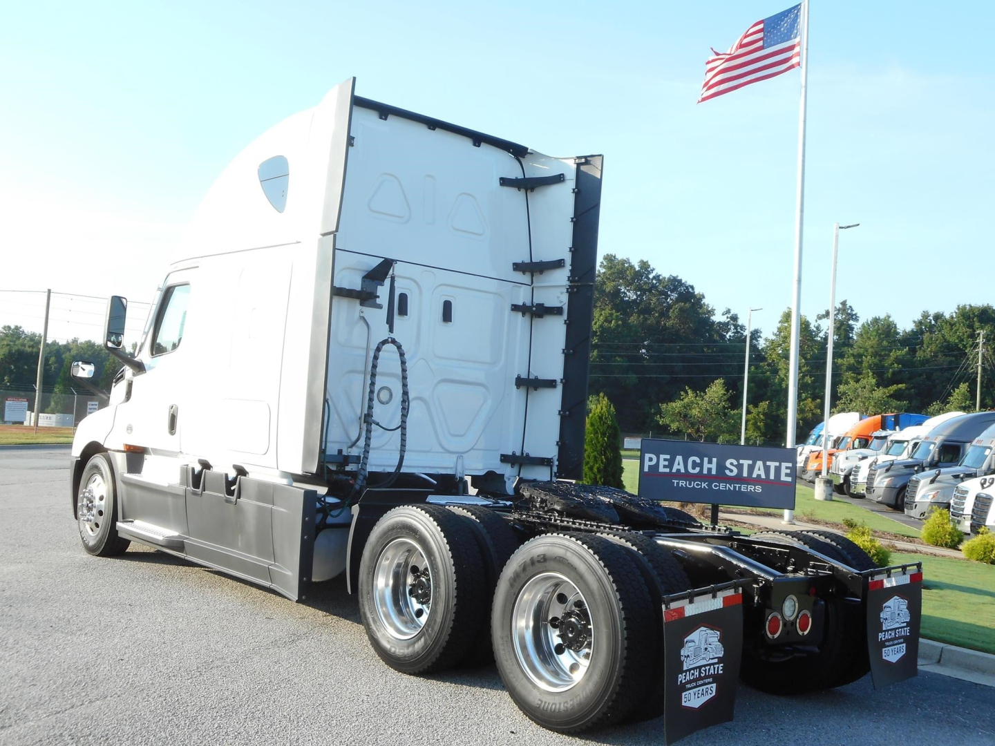 Freightliner Cascadia 126 tractor cab and rear dual axle chassis, side view, with American flag and Peach State Truck Center signage in lot.