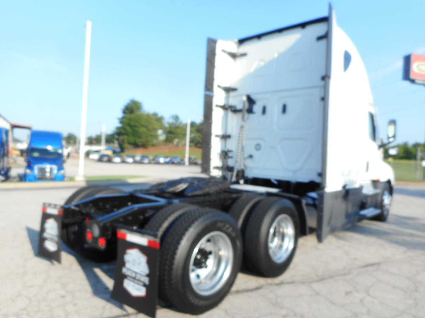 Freightliner Cascadia 126 tractor in a lot, rear and side view showing sleeper cab and dual rear axles with mud flaps.