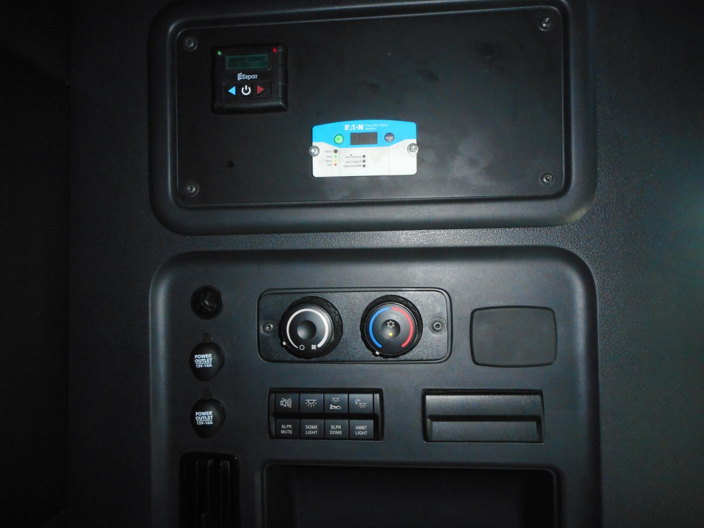 Dashboard panel of Freightliner Cascadia showing control switches, two circular knobs, and a small blue and white security device; upper panel with a power switch and fuse box.