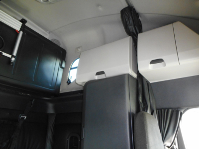 Cab interior of a Freightliner Cascadia sleeper showing storage cabinets and bunk area view.