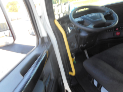 Truck cab interior showing steering wheel and driver's seat of a Freightliner Cascadia with yellow grab handle and door panel.