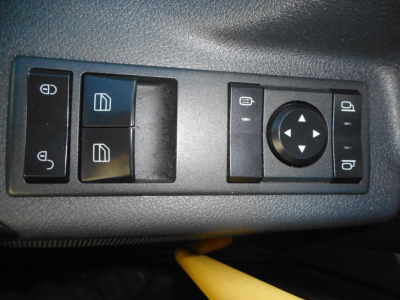 Panel of Freightliner Cascadia door/window controls: four buttons for window operation, two memory/lock icons, circular joystick-like control with arrows for mirror adjustment, and additional side tab switches.