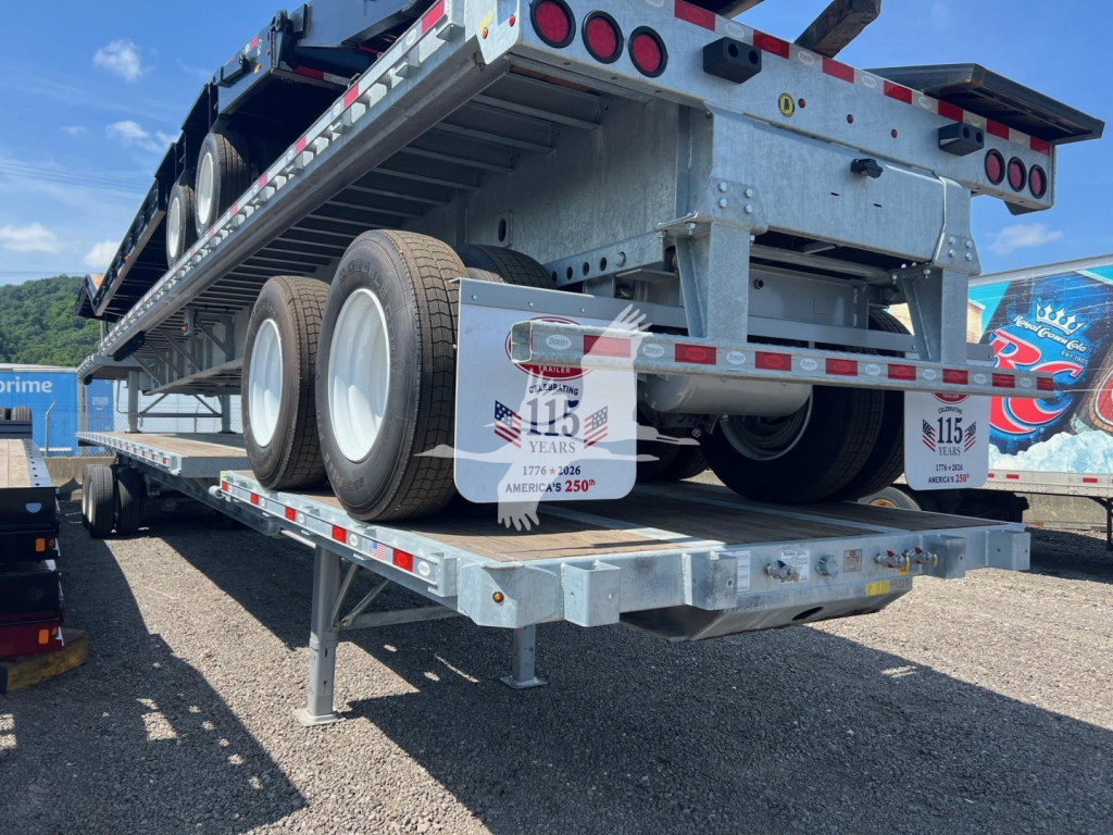 Flatbed trailer with extendable section showing dual rear axles and mud flaps with number stickers, ISO container-style frame, and reflective tape along edges.