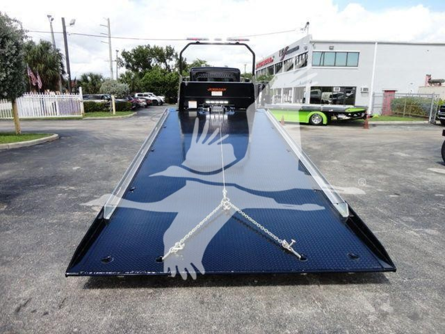 Peterbilt 337 rollback flatbed truck in a parking lot, front view of the long blue steel platform with tie-down chains and winch area.
