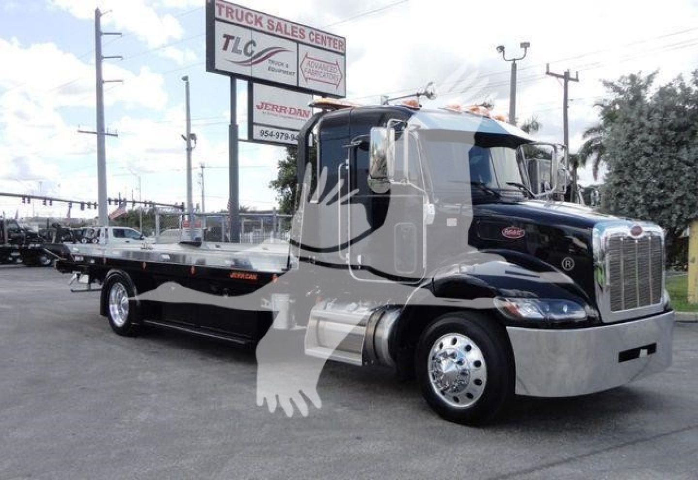 Peterbilt 337 rollback tow truck side view showing flatbed on black and chrome truck with large chrome grille and company signage in background