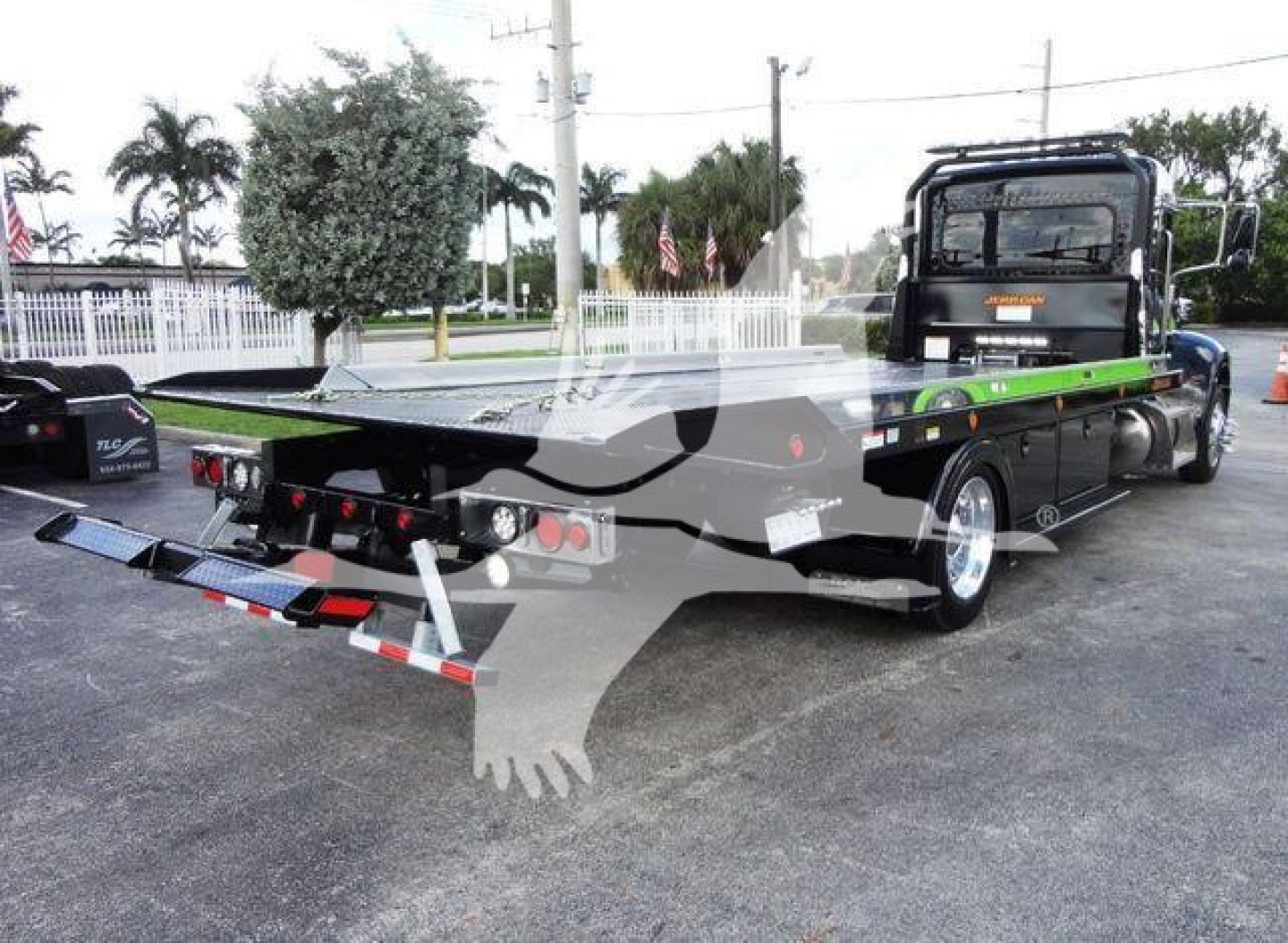 Peterbilt 337 rollback tow trucks chassis seen from rear right, flatbed with green rails, black cab, multiple rear lights and towing equipment visible
