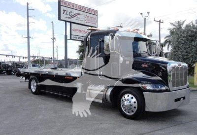 Peterbilt 337 rollback tow truck side view showing flatbed on black and chrome truck with large chrome grille and company signage in background