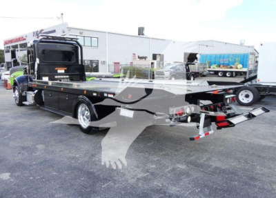 Peterbilt 337 rollback truck in black with loading ramps extended, side rails, and chrome wheels; stock number J03058 visible in background lot.
